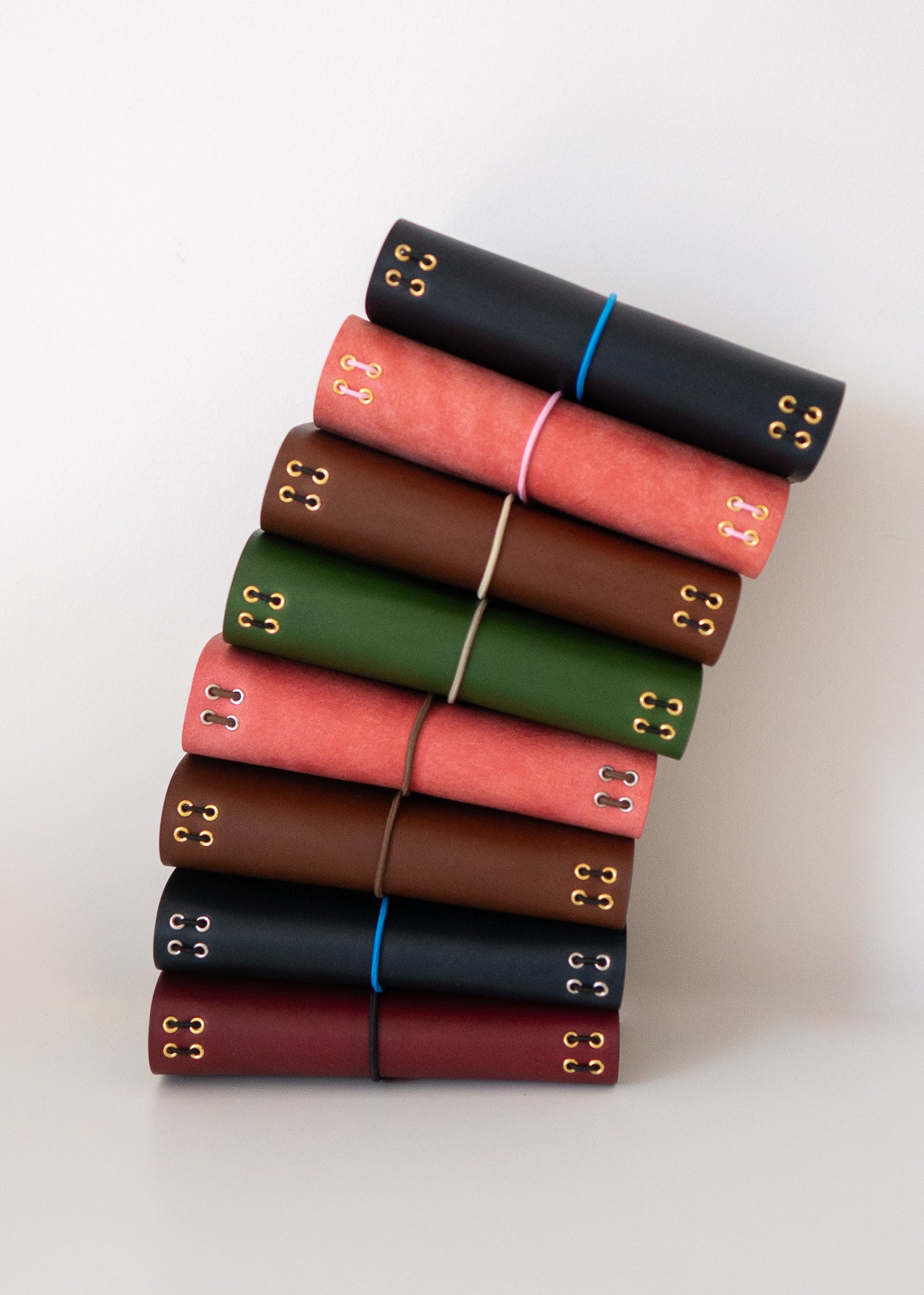 Stack of handcrafted leather notebooks in assorted colors with brass grommets and elastic closures