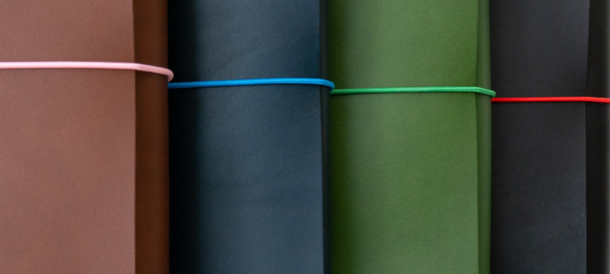 Close-up of four leather traveler’s journals in brown, navy, green, and black with colorful elastic bands and personalized embossing.