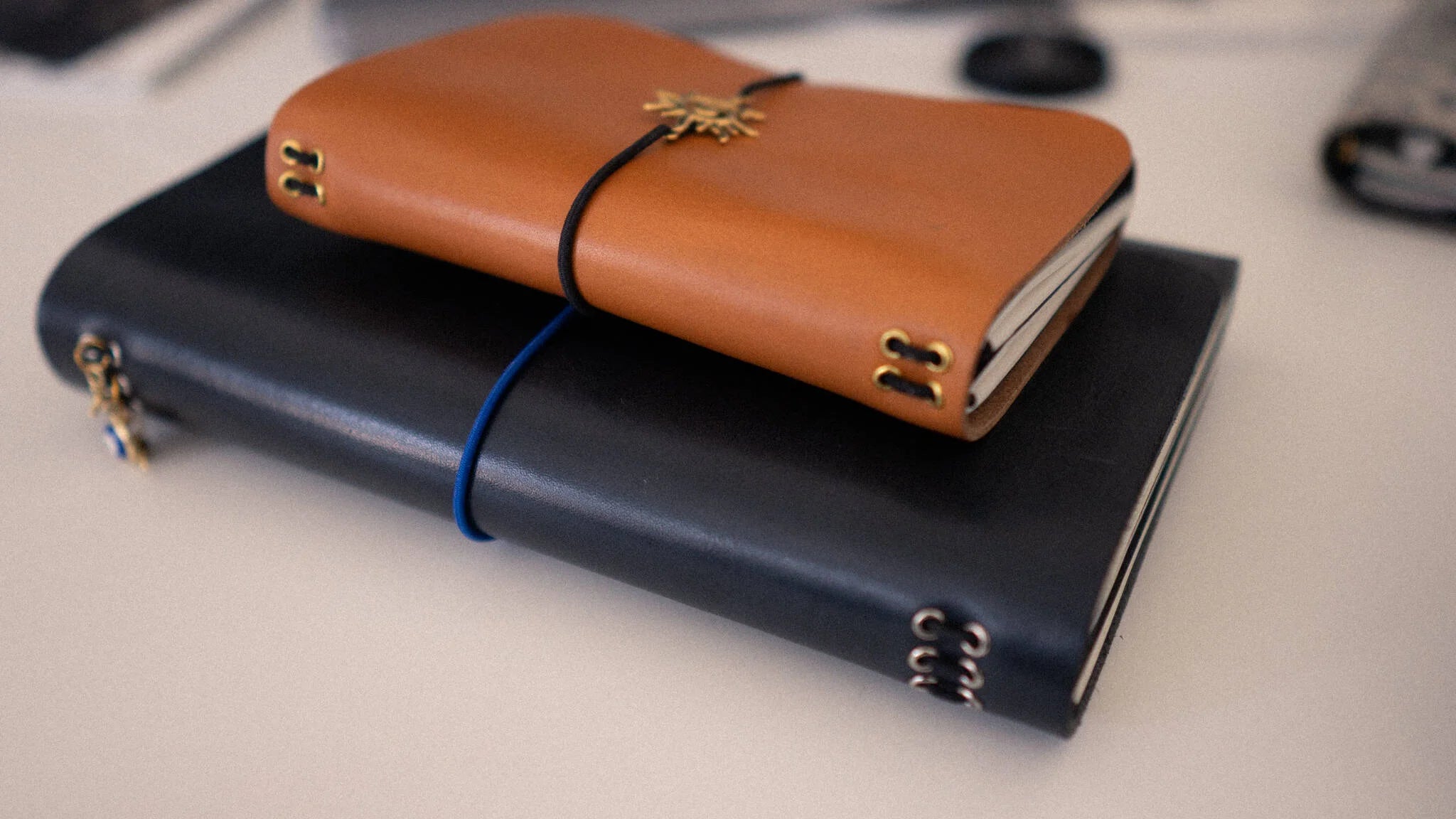 Two leather-bound notebooks, one black and one brown, stacked on a light surface.