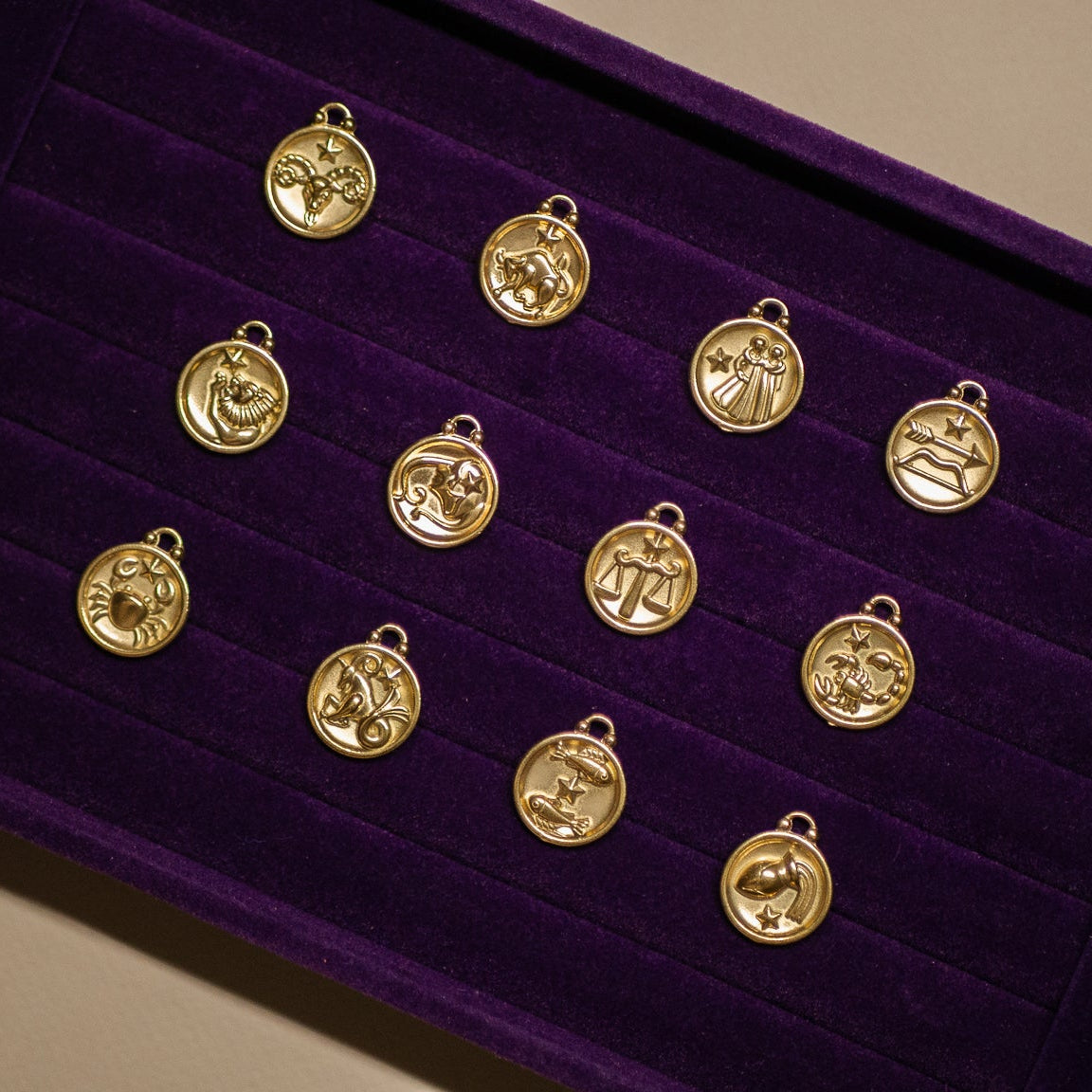 Gold zodiac charm collection on a purple velvet display box